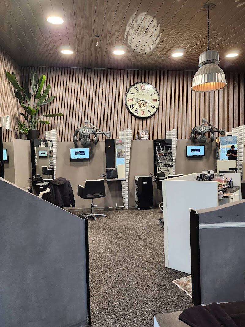De salonvloer met een houten lattenwand, een grote klok en afgeschermde kapplekken met een eigen scherm.